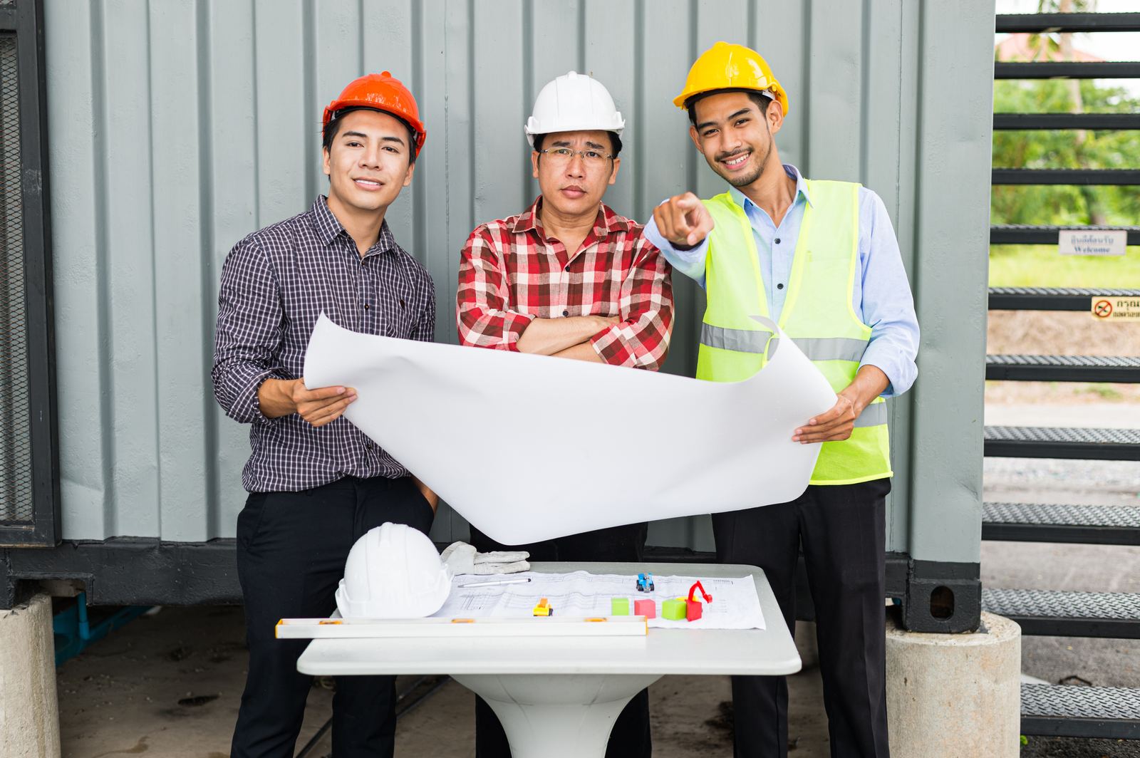 Three site engineers in hard hats reviewing a blueprint together on site